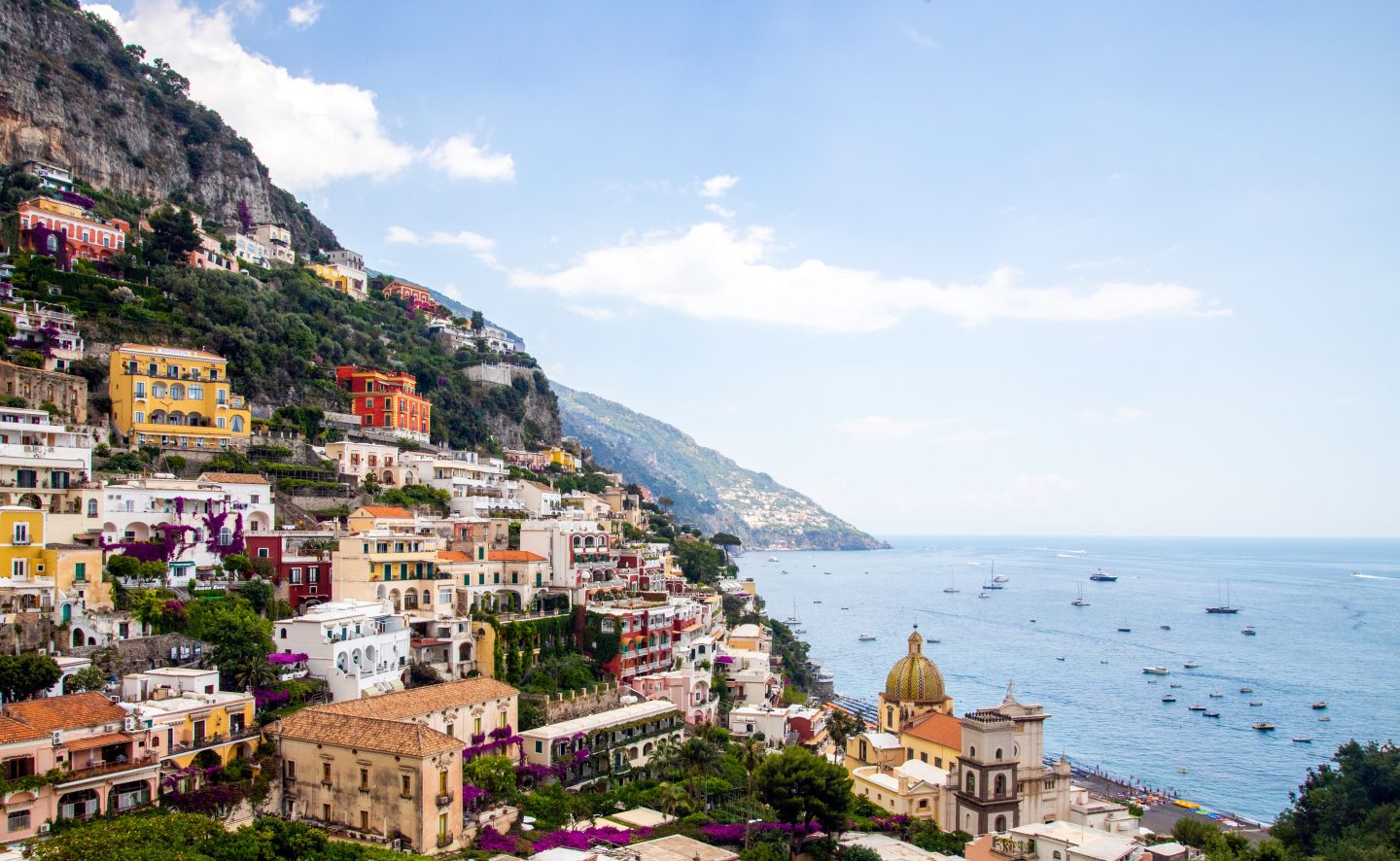 The coast of Italy with building along a tall hill and boats in the sea - one of 2023's best summer destinations.
