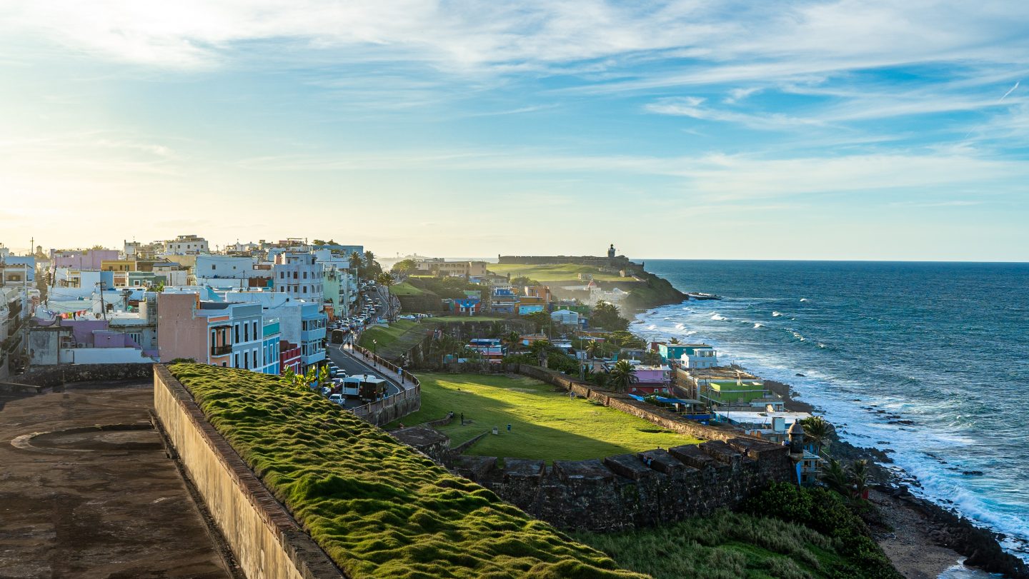 The town of San Juan, Puerto Rico with the ocean to the right and green grass and colorful buildings ahead.