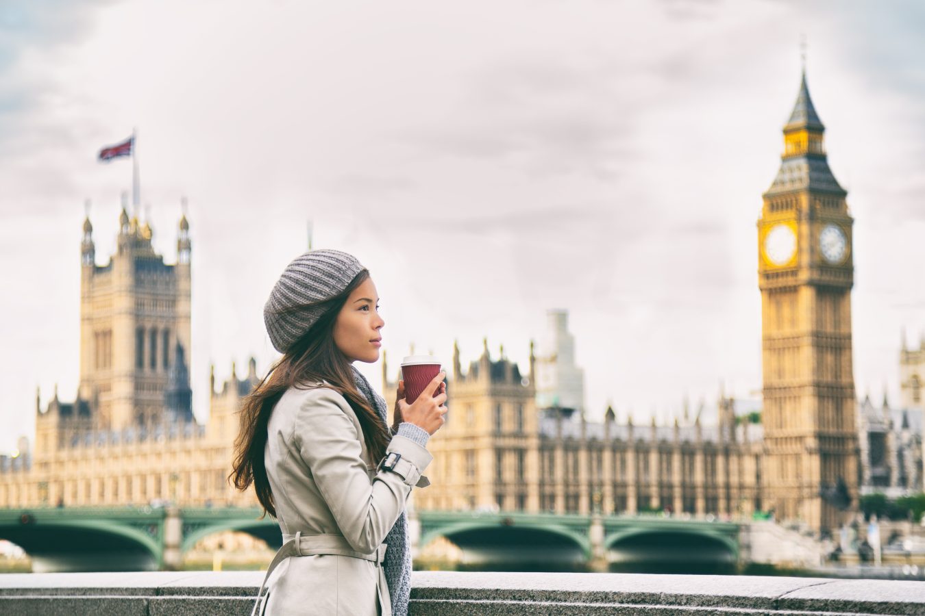 Woman drinking cup of tea with London, England skyline behind her.