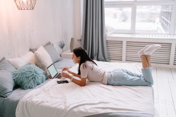 Side view of young asian woman using laptop while lying and resting on bed at home.