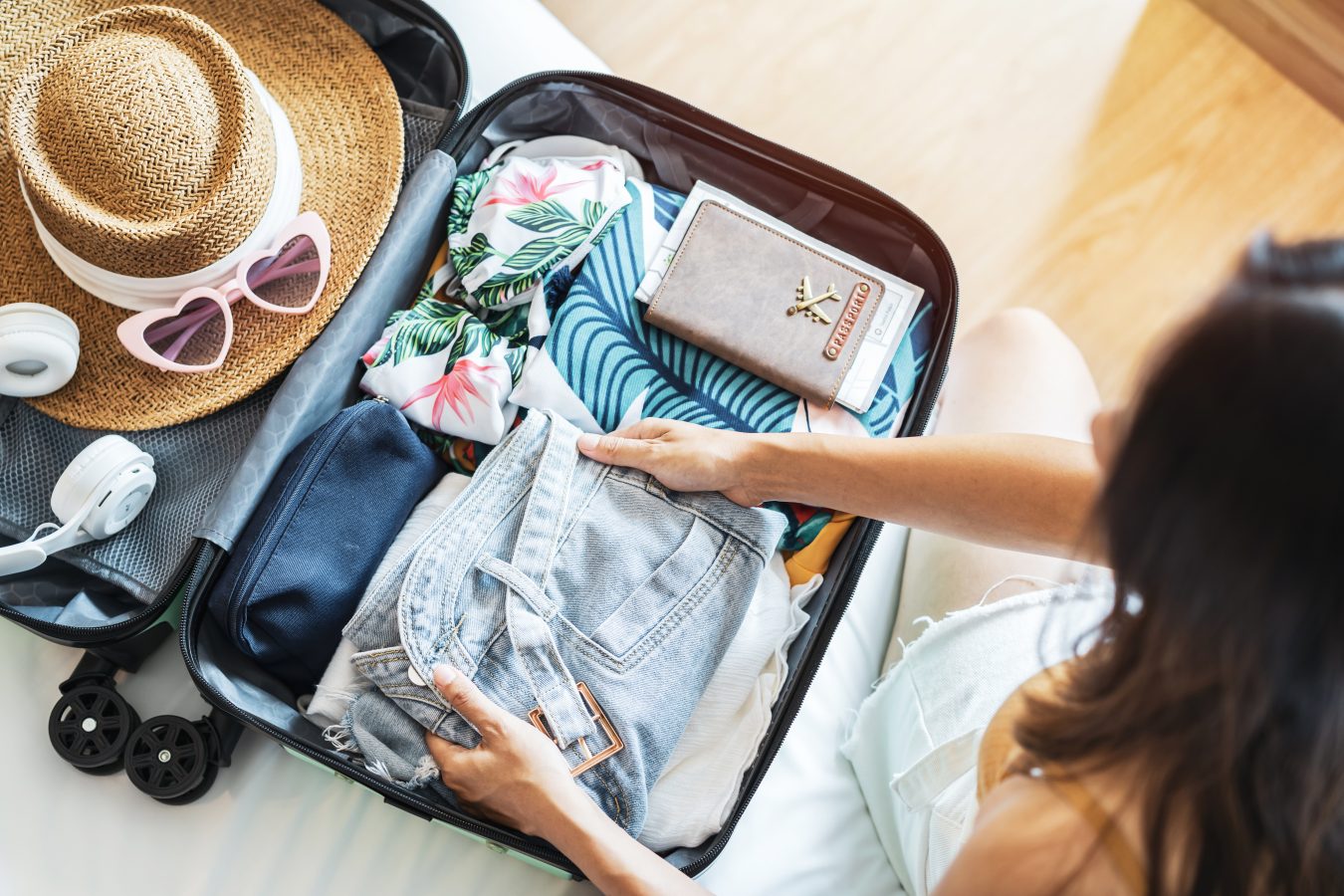 Woman packing her suitcase with warm weather clothes and accessories for spring break.