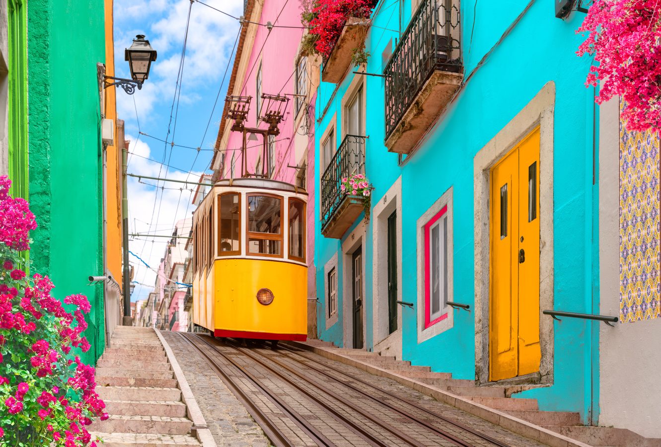 Yellow tram on a street with colorful houses and flowers on the balconies in Lisbon, Portugal.