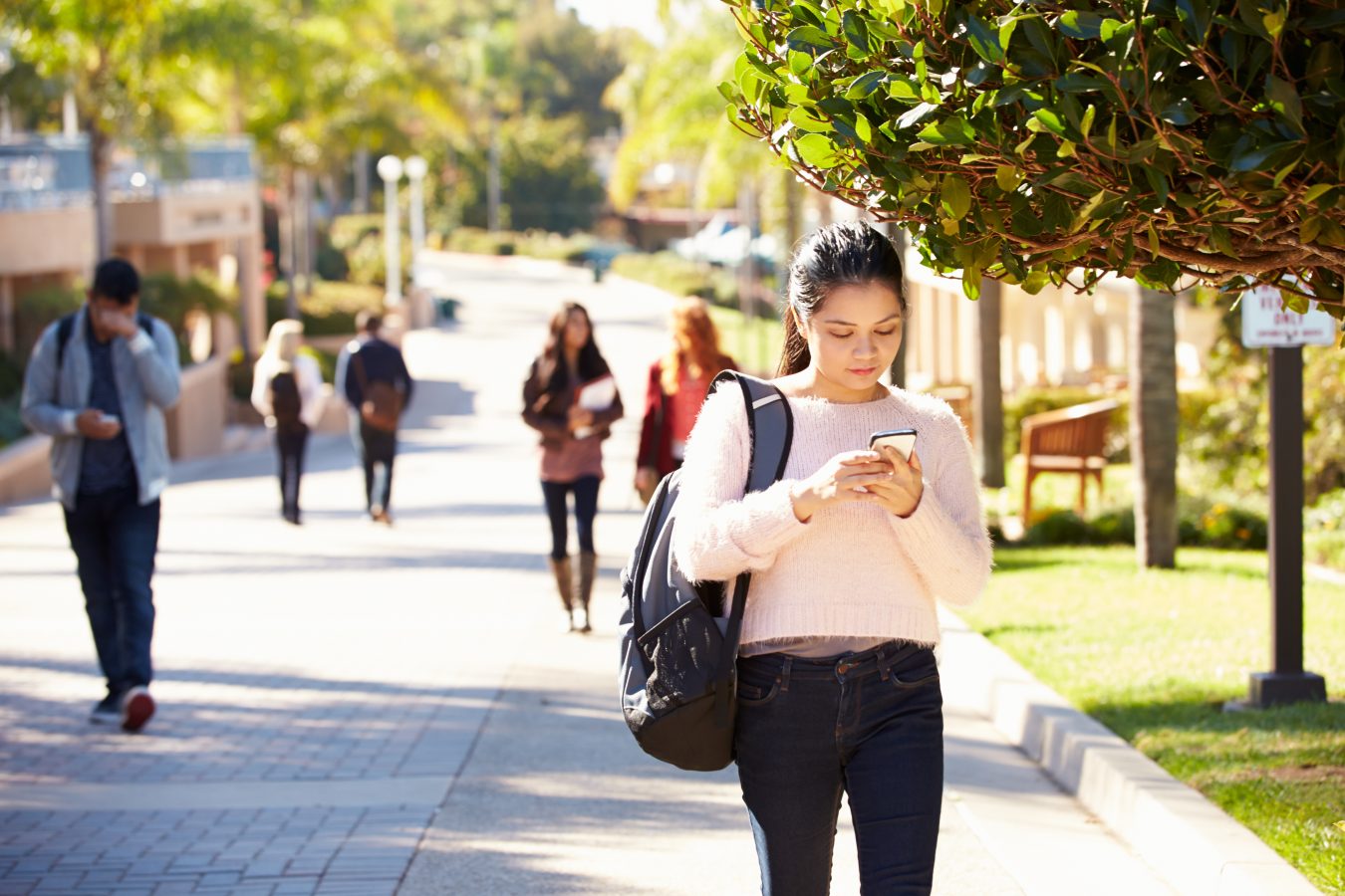 Student walking outdoors on college campus, while on her phone.