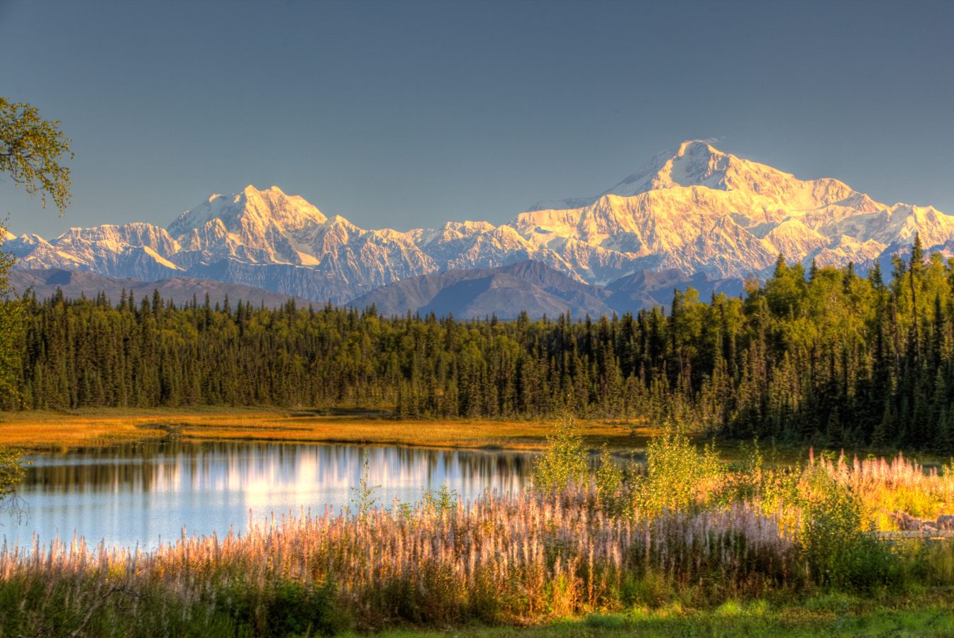 Sunrise on the mountains in Denali National Park, Alaska, USA with a lake in the foreground.