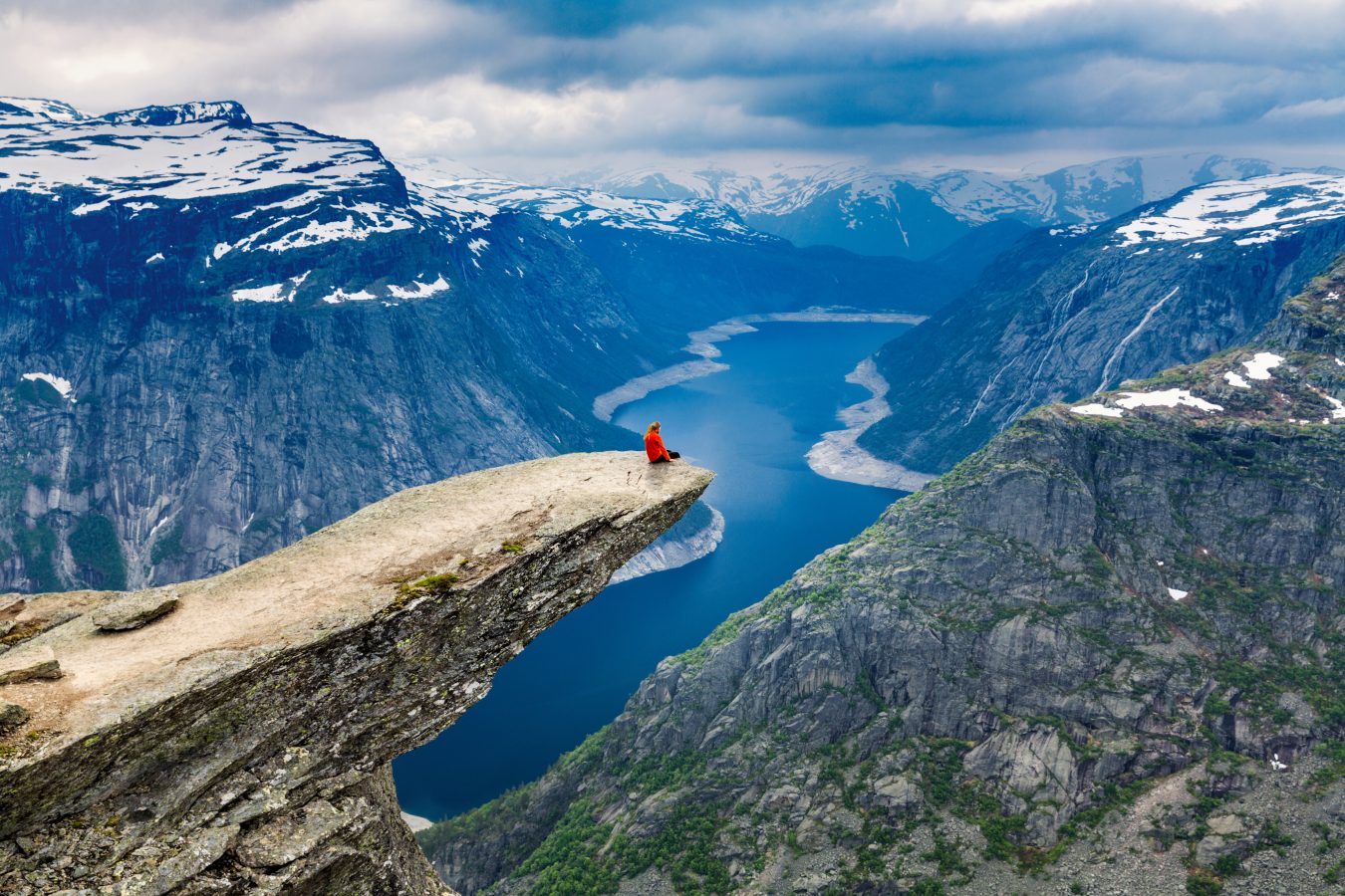 Woman sits on Trolltunga in Noway, meditating in one of the world most relaxing destinations.