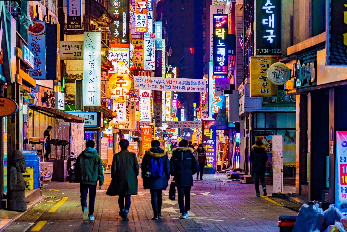 A group of friends walks under the neon lights and signs on a shopping street in Seoul, South Korea.