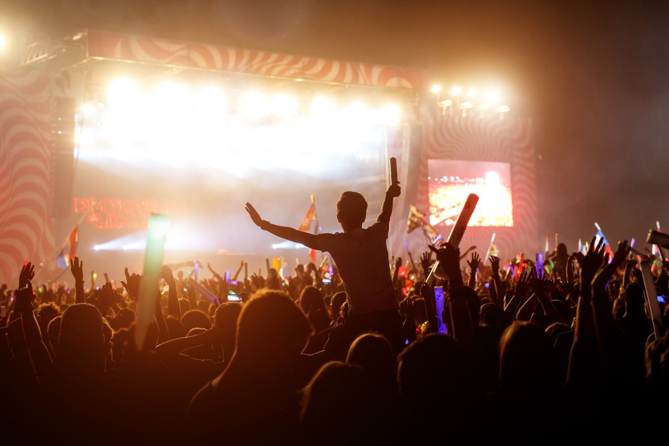 Silhouette of a young man above the crowd at a concert or big festival event.