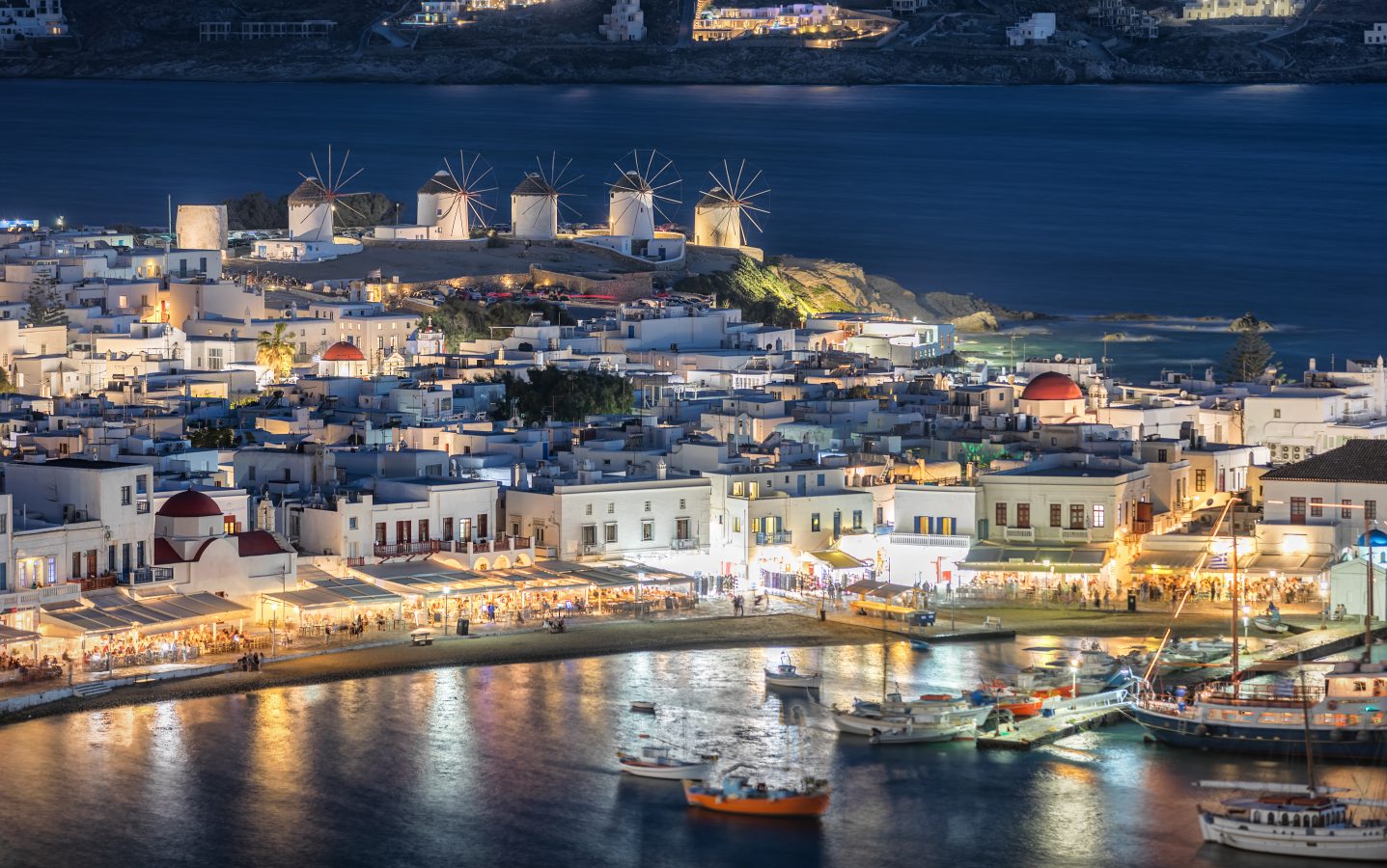 Mykonos, Greece lit up at nighttime with a large crowd of the nightlife scene along the coastline.