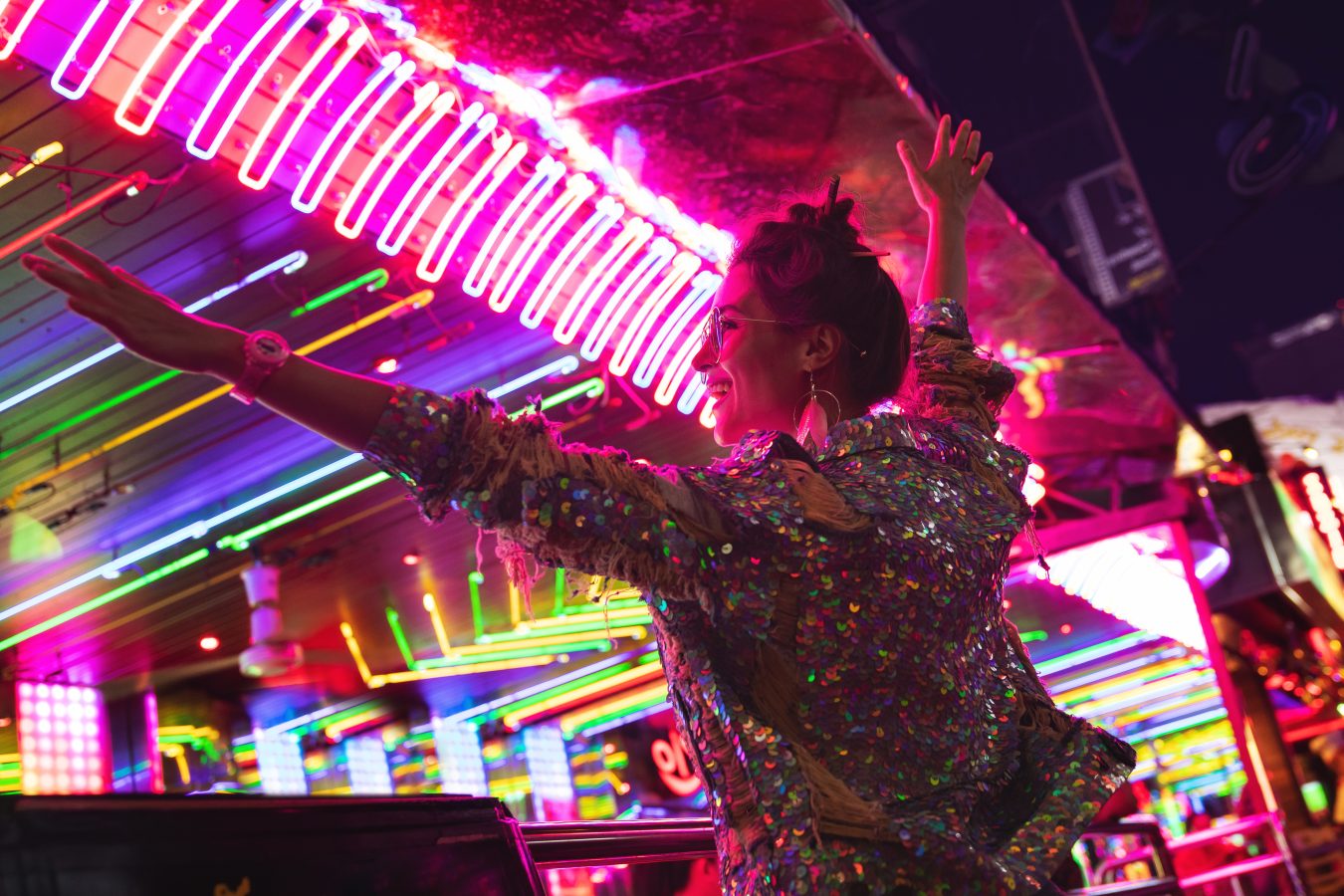 A young woman dances, backlit by the neon signs of the party scene she is at - like in Thailand, one of the world's top party destinations.