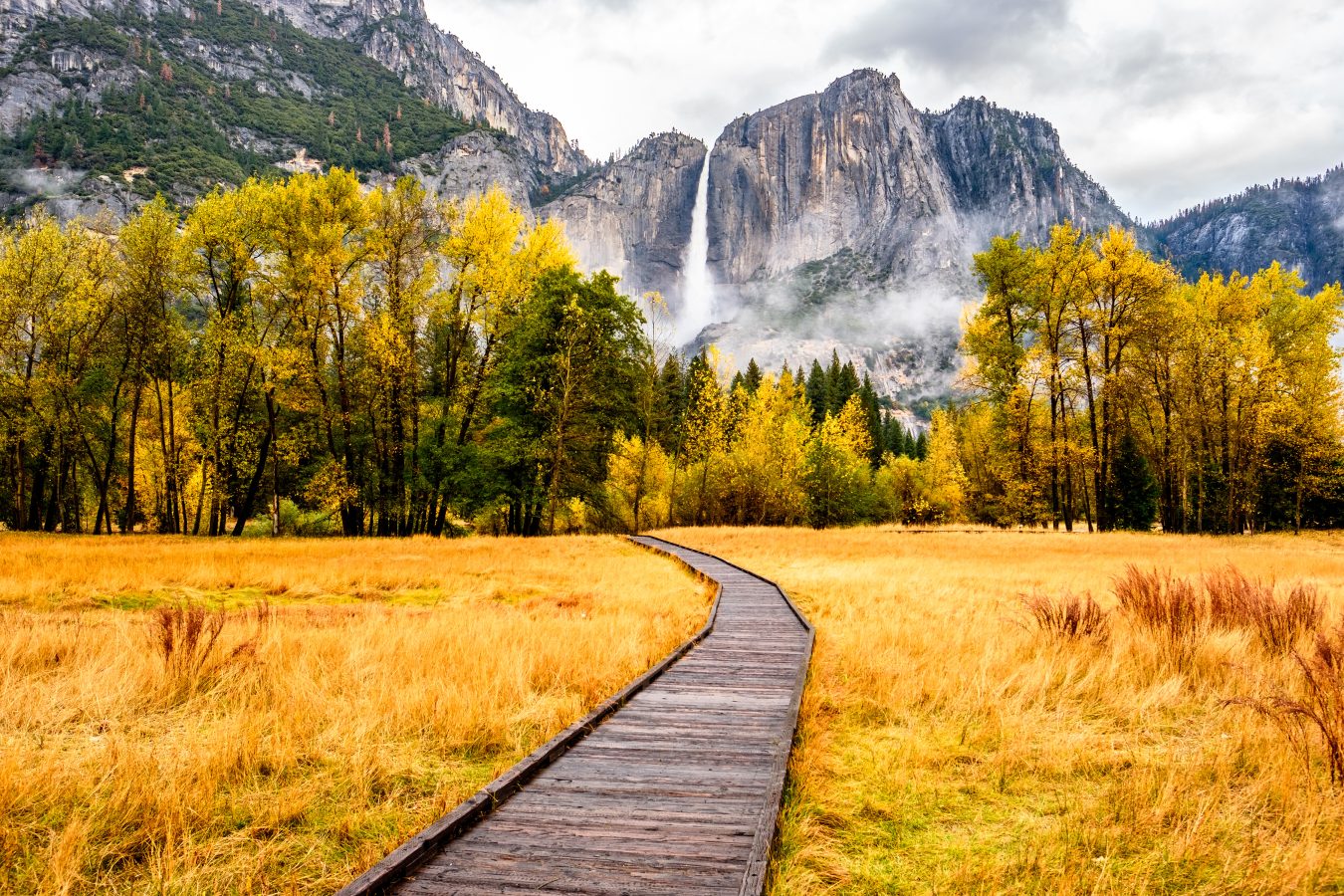 Meadow with boardwalk in Yosemite National Park Valley with Yosemite Falls at cloudy autumn morning.