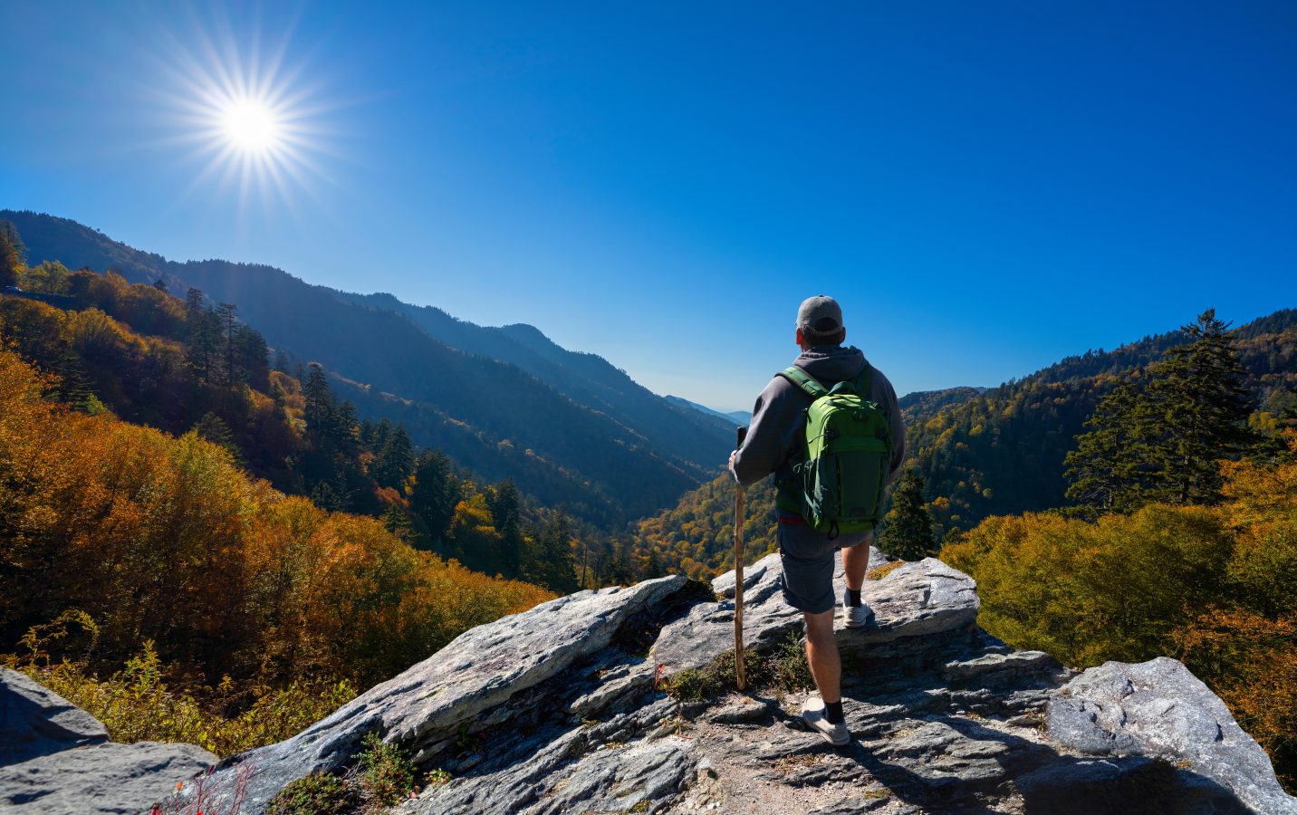 Hiker stands atop a mountain, overlooking the valley of a clear sunny autumn day - taking in the peace and solitude.