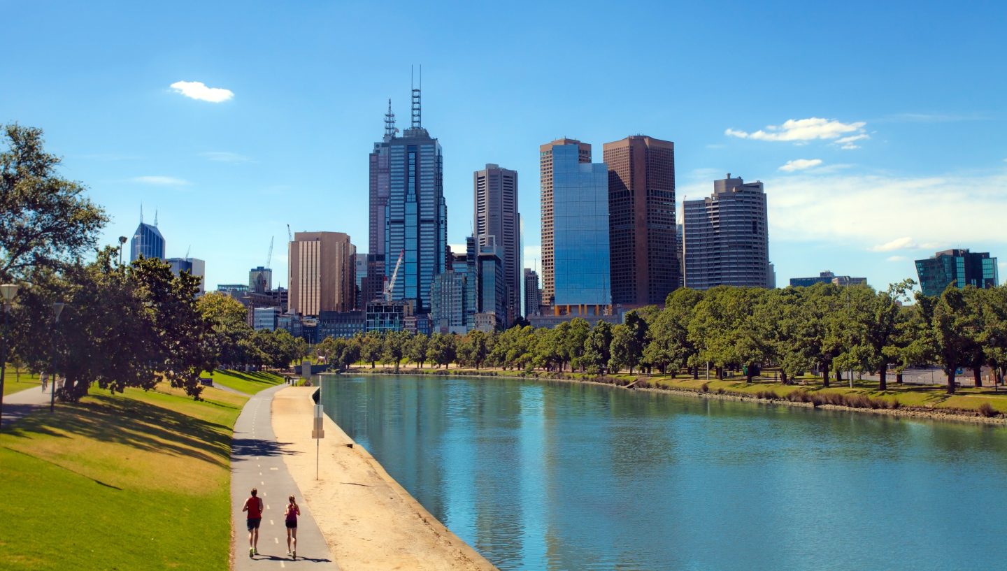 People walk along the water with the Melbourne, Australia city skyline in the background.