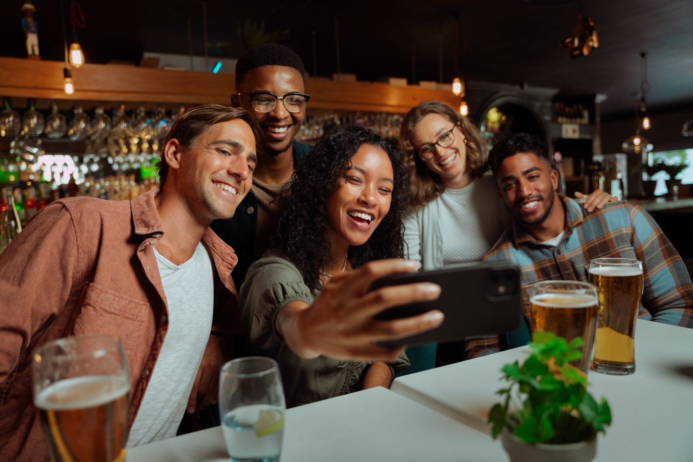 Group of young adult friends eating dinner at restaurant taking selfie with phone.