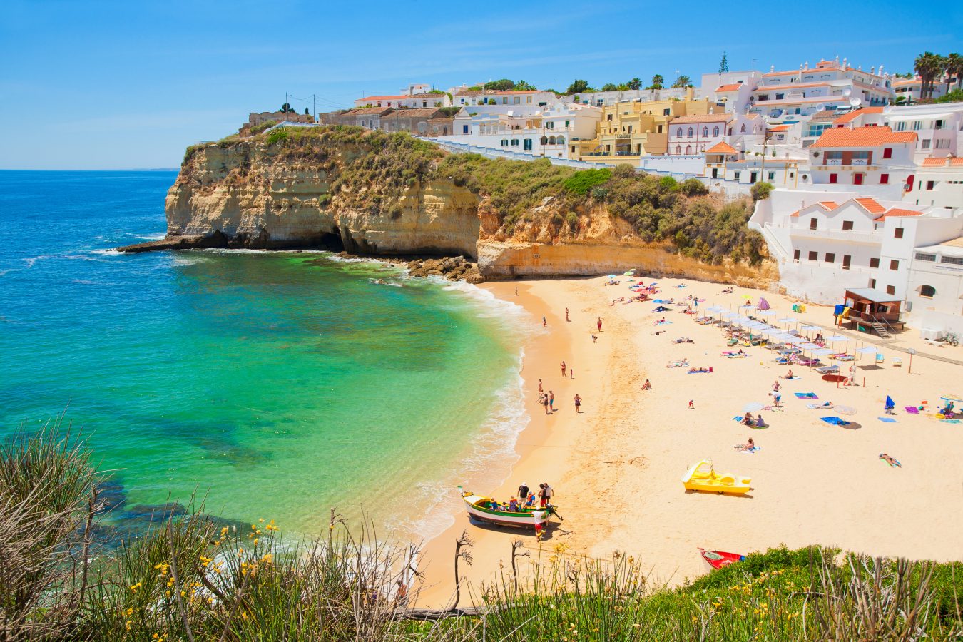 A beach in Algarve, Portugal with bright waters, light sand, and the European city in the hills behind.