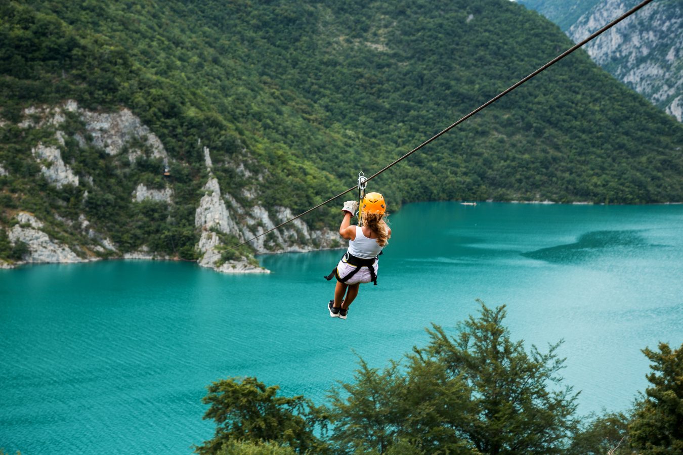 A traveler sliding on a zip line over a bright blue lake - taking on the fun and adventure of gap year travel.