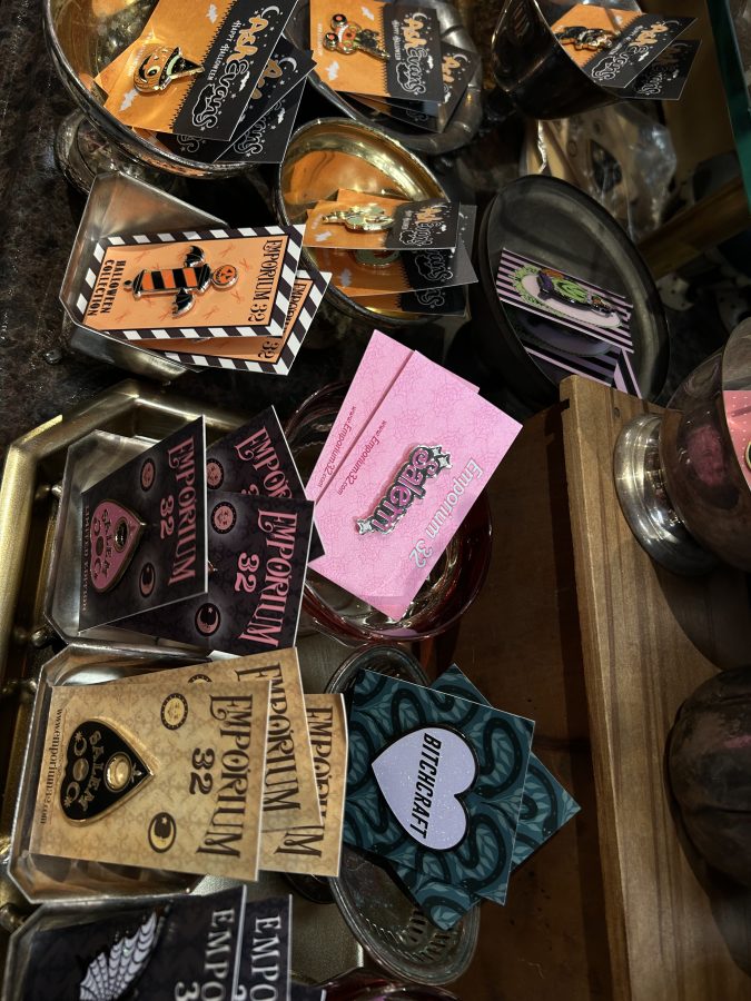 Some pins for sale in a shop, Emporium 32, in Salem, Massachusetts. They include a Barbie styled pin that reads Salem, ouija board planchettes in a different colors, and more.