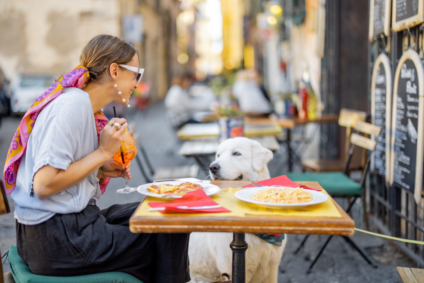 A young woman sits outside an Italian cafe with her dog while on a study abroad experience.