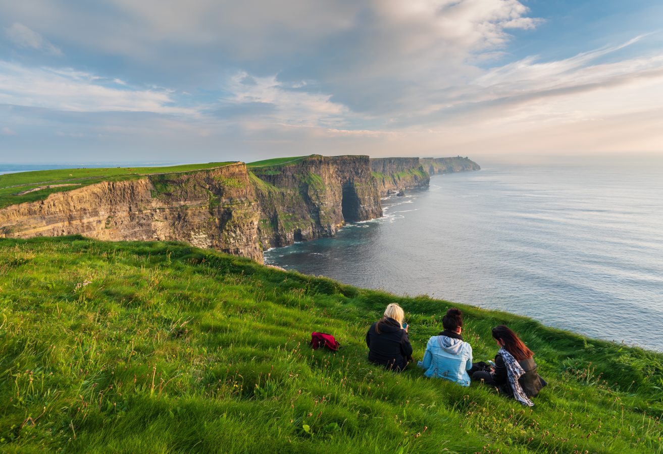 Group of girls sitting on the edge of the Cliffs of Moher in Ireland.