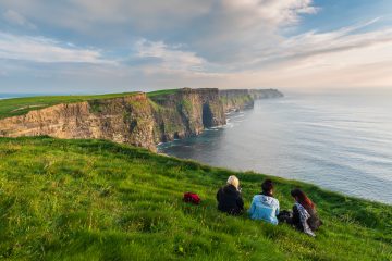 Group of girls sitting on the edge of the Cliffs of Moher in Ireland.