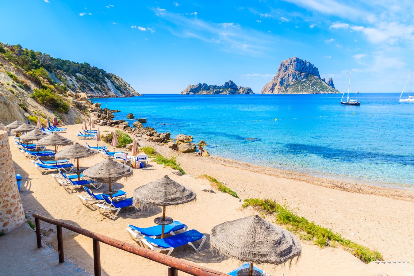 View of Cala d'Hort beach with sunbeds and umbrellas and beautiful azure blue sea water, Ibiza island, Spain (one of the best spring break destinations).