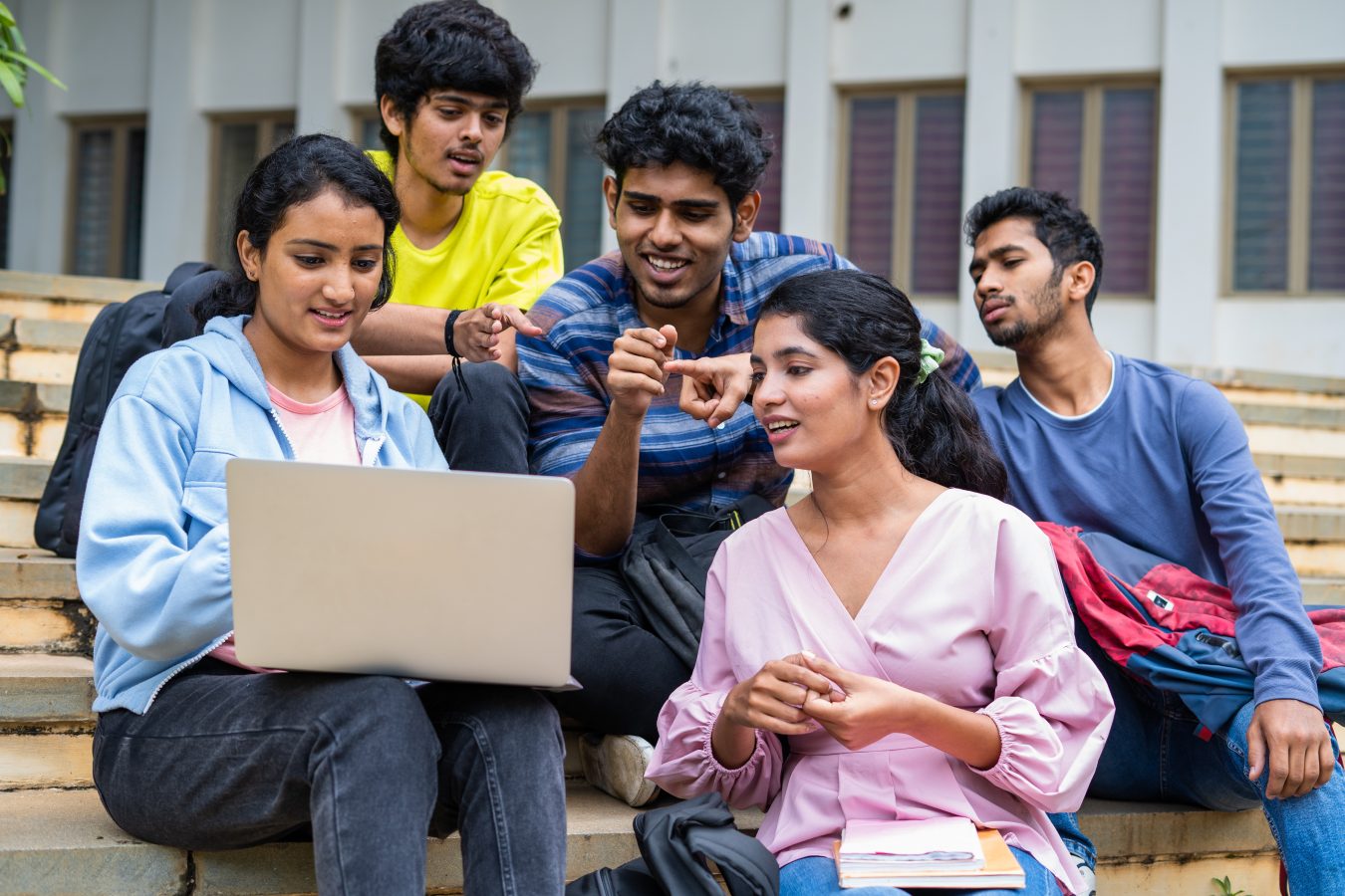 Group of Indian students sit around a laptop on a their college campus.