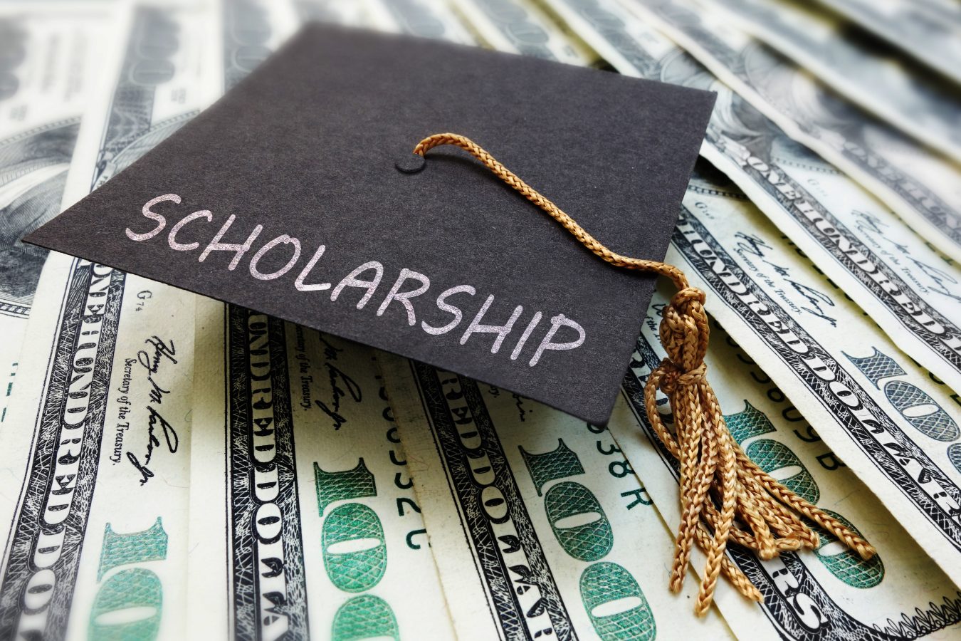 Grad cap with "scholarship" written across it sitting atop $100 bills.